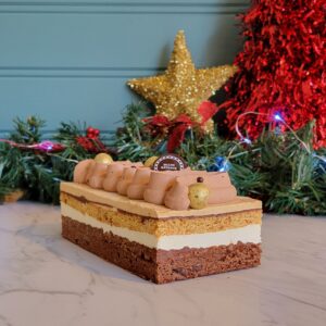 Bûche décadente composée d'un brownies chocolat, croustillant praliné amande-noisette, bavaroise à la vanille, financier aux biscuits graham maison, ganache au chocolat noir, mousse au praliné amande-noisette et couronné de chantilly au chocolat noir.